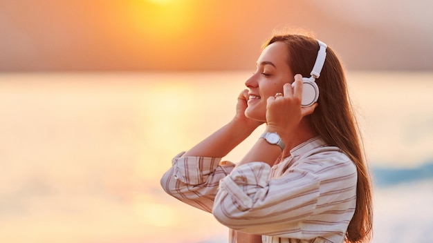 Calma serena mulher sozinha com os olhos fechados gosta de ouvir relaxar música itinerante à beira-mar na hora do pôr do sol Feliz lindo momento de vida