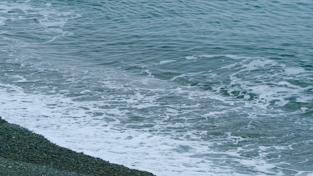 Calma superfície do mar borrada ondas espumosas suaves lavando praia de seixos ainda