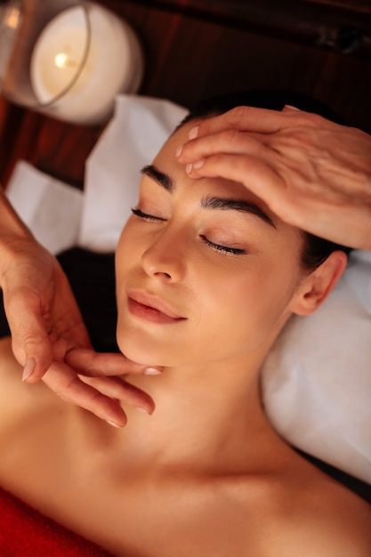 Foto calmado y relajado. atractiva clienta impecable que participa en un masaje meditativo con velas perfumadas