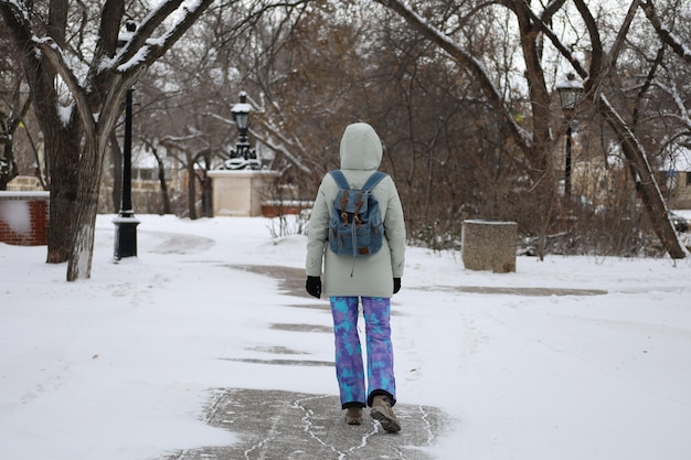 Calmamente vestida para o clima severo canadense uma menina em calças de esqui no fundo de um parque de inverno