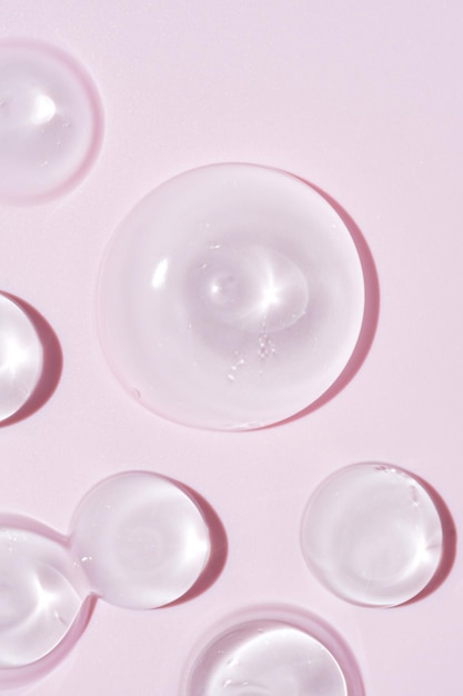 Calmar la crema, la loción, la crema hidratante, las manchas de gel sobre fondo rosa, el cuidado de la piel y el producto de belleza corporal, las manchas cosméticas de gel líquido.