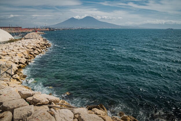 Calmo azul Tirreno Vista do mar do aterro de Nápoles para o vulcão do Monte Vesúvio Curvas de quebra-mar de pedra ao longo do mar