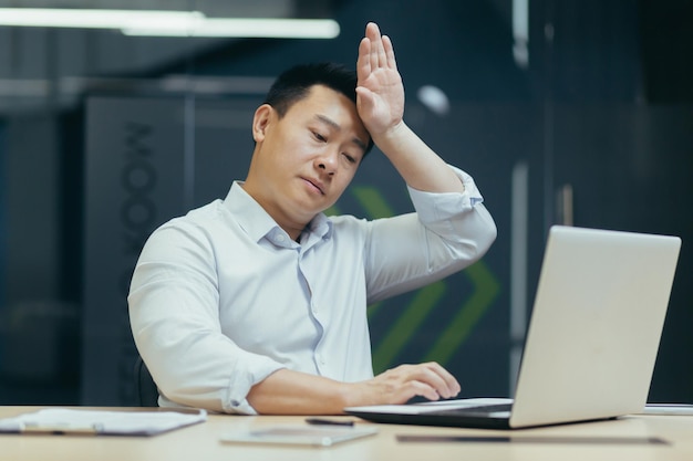 Calor e falta de ar no escritório um homem asiático trabalha em um laptop está quente e não há ar