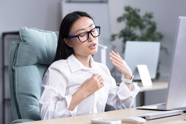 Calor en la oficina mujer asiática tratando de refrescar a la mujer de negocios que trabaja en la computadora saludando