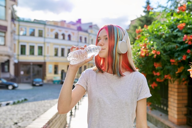 Calor de verano en la ciudad mujer joven con botella de agua adolescente en auriculares bebiendo agua en un día soleado en una calle de la ciudad