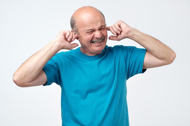 Calvo hispano senior tapando los oídos con los dedos escuchando fuertes sonidos de música