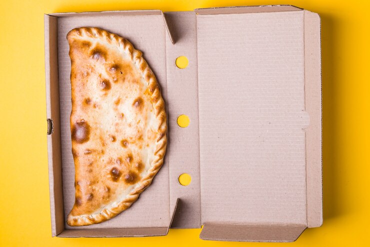 Foto calzone de pizza fechado em uma caixa de embalagem em um fundo amarelo.