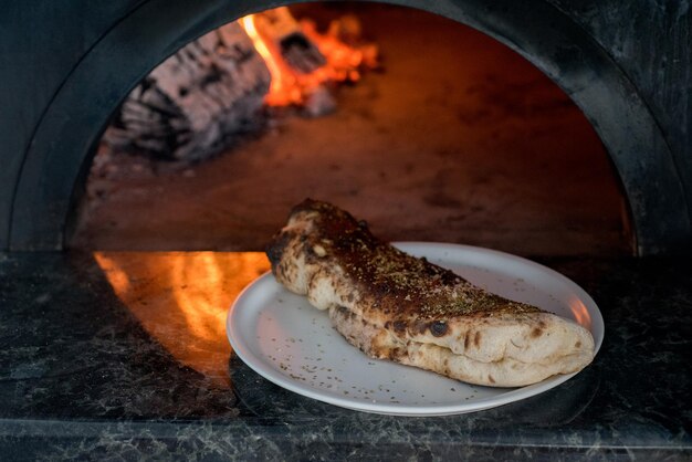 Calzone-Pizza auf einem Teller, Nahaufnahme Neapolitanischer traditioneller Holzofen