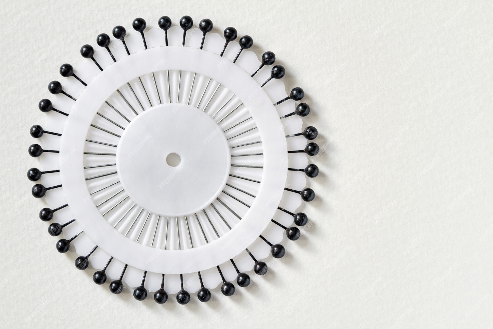 Cama aguja blanca con alfileres negros sobre fondo blanco. juego de alfileres con cabeza negra. primer plano, enfoque selectivo, superior | Foto Premium