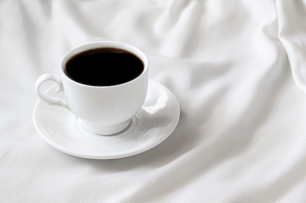 en la cama blanca hay una taza blanca con café negro