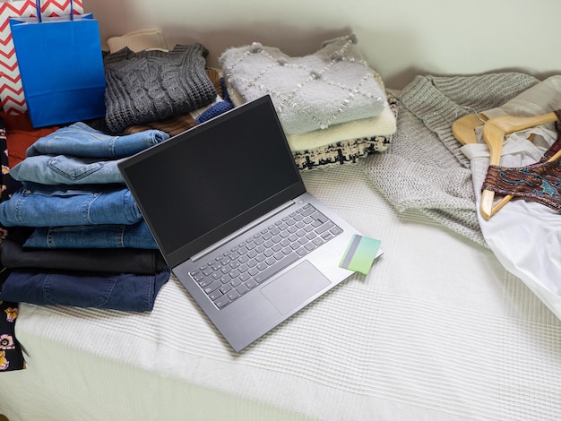 Cama cheia de sacos de compras de roupas, um laptop e um conceito de compras na Internet de cartão de crédito