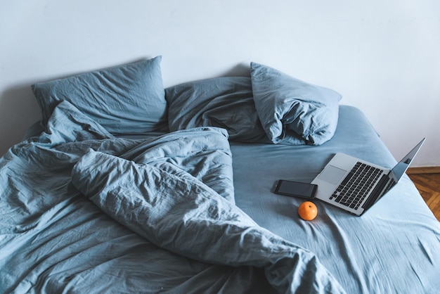 Cama cinza bagunçada vazia com laptop. conceito de estilo de vida descanso na cama