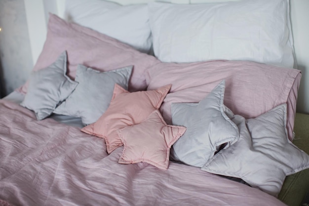 Cama com roupa de cama rosa e cinza e almofadas em forma de estrela