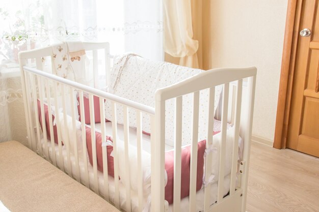 Foto cama de bebé com almofadas brancas e de cor borgonha com atacadores