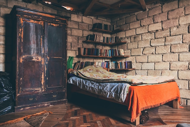 Cama de solteiro com prateleiras surradas de guarda-roupas com livros no canto contra o fundo de uma parede