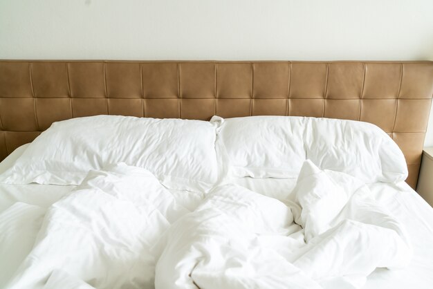 Foto cama desordenada con almohada blanca y manta en la cama