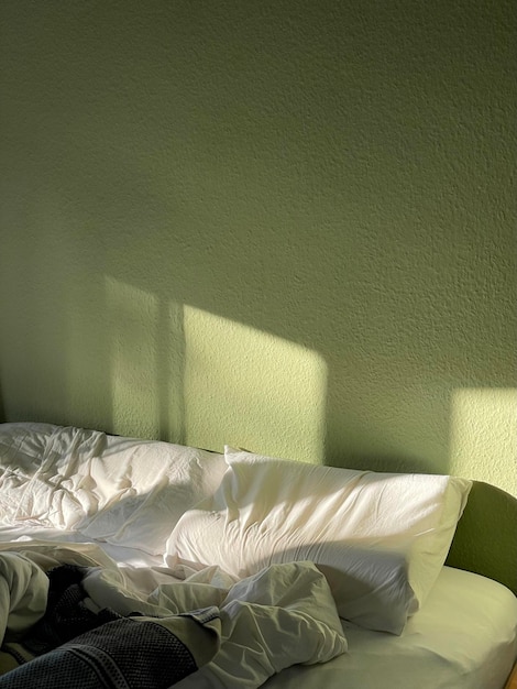 Cama desordenada junto a una pared verde en el dormitorio bajo la luz del sol