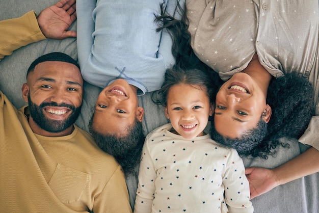 Cama familiar feliz y retrato de niños relajados o felices con los padres juntos por la mañana en un dormitorio. Papá y mamá sonrientes disfrutan de tiempo de calidad con niños o niñas con felicidad, cuidado y amor.