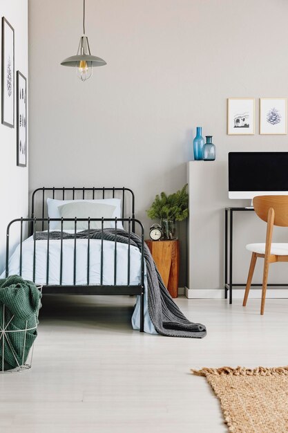 Cama industrial individual con ropa de cama azul en un elegante espacio de copia de dormitorio gris en una pared vacía