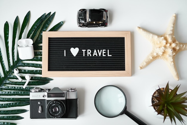 Foto cama plana de viagem. câmera, máscara protetora, fones de ouvido, placa com a inscrição adoro viajar em branco