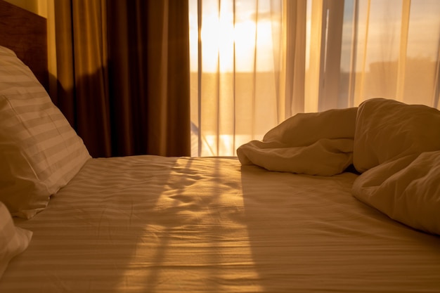 Cama con sábanas blancas al amanecer Lugar para dormir con almohadas y una manta al amanecer