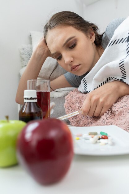 En la cama yace una adolescente y delante de ella hay una mesa con manzanas y medicinas que deben ser tragadas