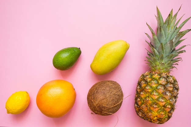 Camada plana com frutas tropicais em rosa: coco, abacaxi, manga, grapefruit, limão, abacate
