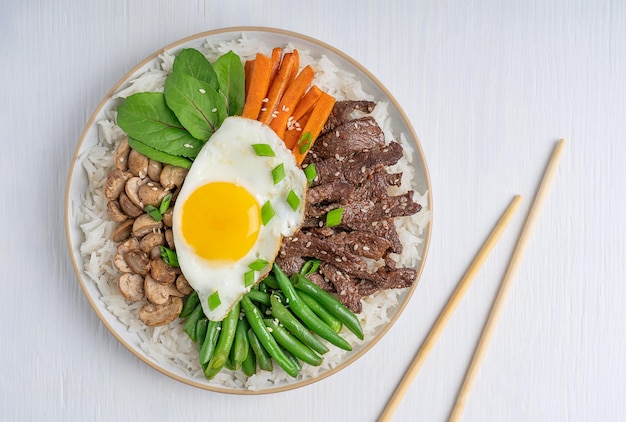 Camada plana de Bibimbap coreano feito de arroz cozido coberto com fatias de carne, vegetais e ovo frito