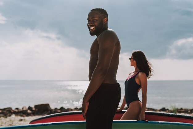 Cámara afroamericana joven de la persona que practica surf que presenta en la playa.