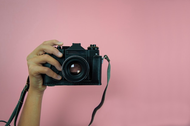 Cámara antigua en una mano femenina sobre un fondo rosa