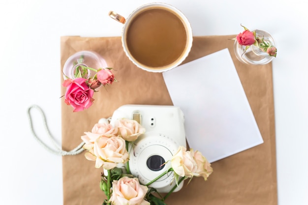 Cámara blanca en el escritorio entre las flores junto a una taza de café.