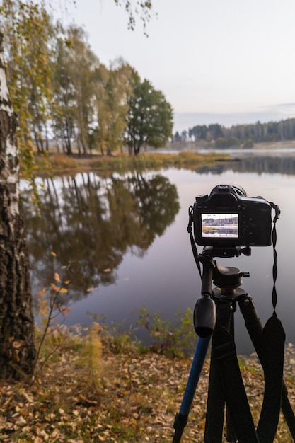 Cámara digital negra en trípode disparando paisaje matutino brumoso temprano en el lago de otoño con enfoque selectivo