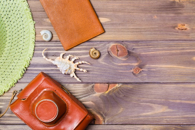Cámara en un estuche, pasaporte, sombrero y conchas marinas sobre un fondo de madera