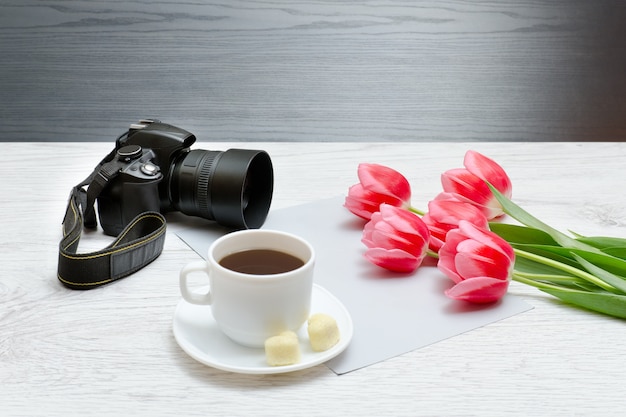 Cámara fotográfica, taza de café y tullips rosas. Fondo de madera