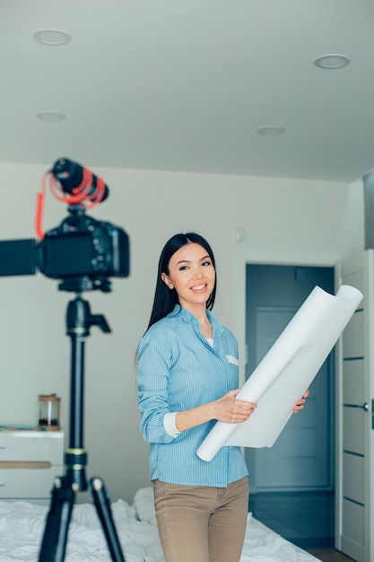 Cámara y micrófono en trípode en el dormitorio Joven arquitecto blogger confiado grabando un video y sonriendo