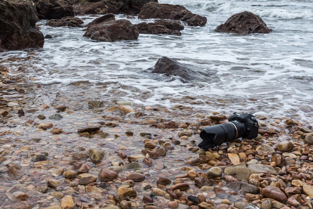 Cámara réflex digital en la playa de piedra húmeda de agua mar ola