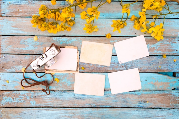 Cámara retra y viejo álbum de foto de papel instantáneo vacío en la tabla de madera con las flores.