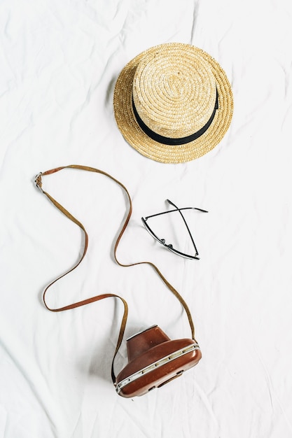 Foto cámara retro vintage, gafas, sombrero de paja sobre superficie blanca