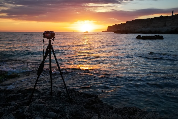 Cámara sobre un trípode en la playa durante una hermosa puesta de sol ardiente