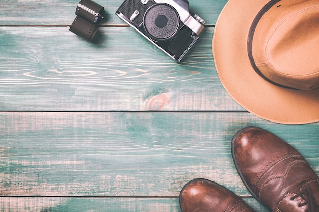 Cámara vintage con película, zapatos marrones y sombrero fedora sobre fondo de madera verde.