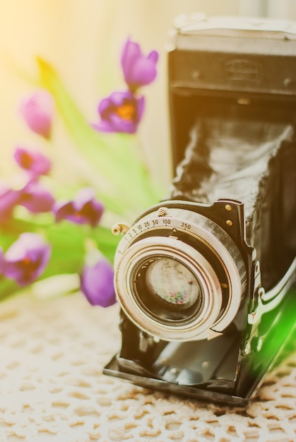 Foto cámara del vintage con el ramo hermoso de flores en mantel hecho punto. viejo concepto de bodegón vintage