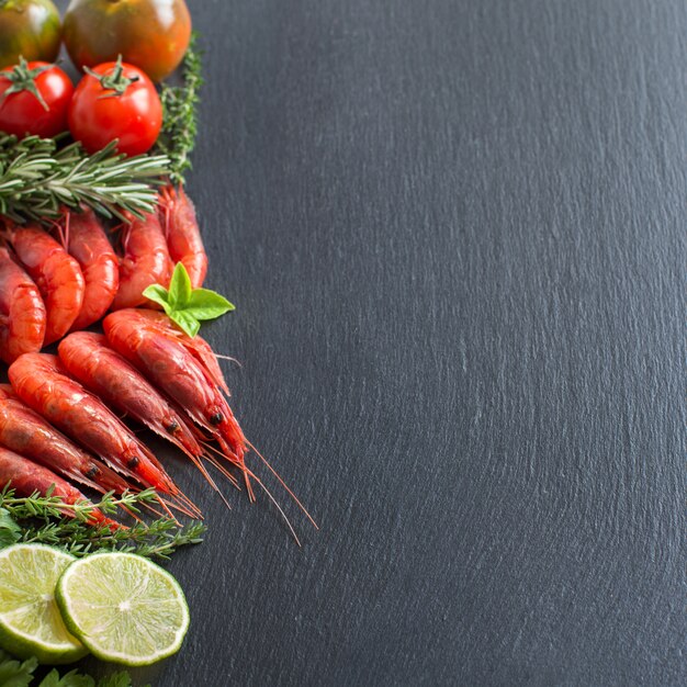 Camarão cru com tomate, limão e ervas na mesa escura, close-up