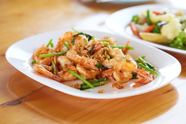 Camarão frito com alho e legumes em chapa branca em frutos do mar de mesa de madeira