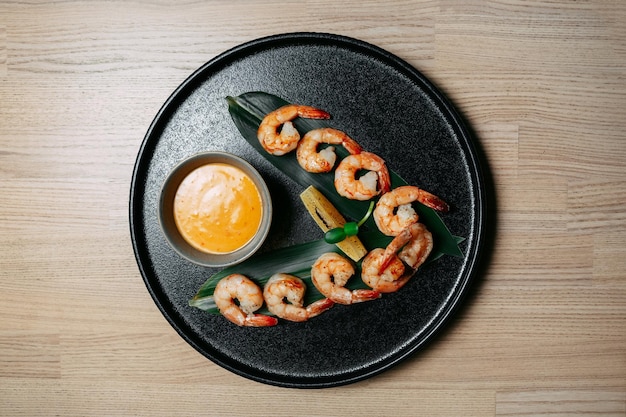 Camarão frito em uma folha verde com uma fatia de molho laranja e amarelo em uma placa preta sobre um fundo de mesa de madeira