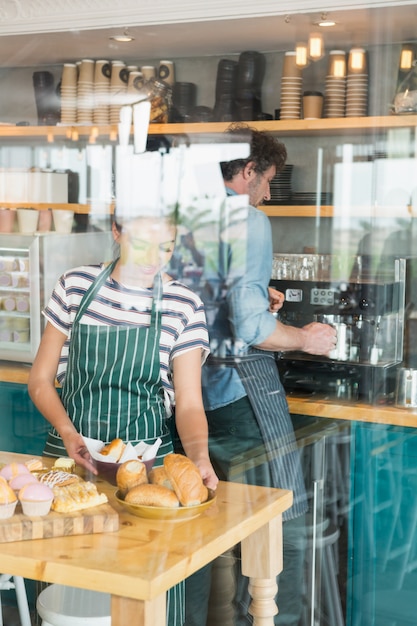 Camarera arreglando postre y merienda en el mostrador mientras el camarero prepara café