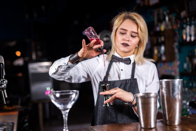 La camarera carismática demuestra el proceso de hacer un cóctel mientras está de pie cerca del mostrador del bar en el pub