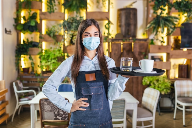 Camarera feliz sosteniendo la bandeja con una taza de café, trabajando en la cafetería y sirve la mesa