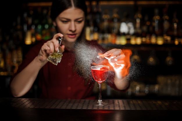 Camarera femenina rociando una copa de cóctel con jeringa Aperol cóctel con un whisky pelado y haciendo una nota ahumada en la barra del bar