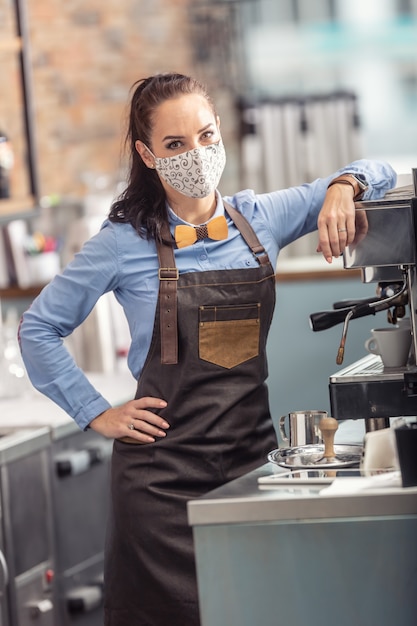 La camarera de moda usa una mascarilla protectora mientras prepara un espresso en una cafetería.