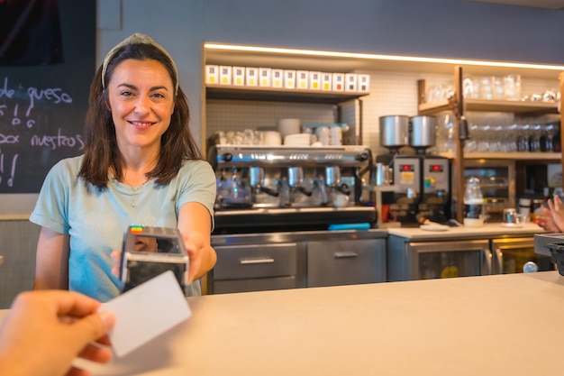 Una camarera morena caucásica sonriendo entregando el datáfono para cargar con el contacto de la tarjeta de crédito del cliente